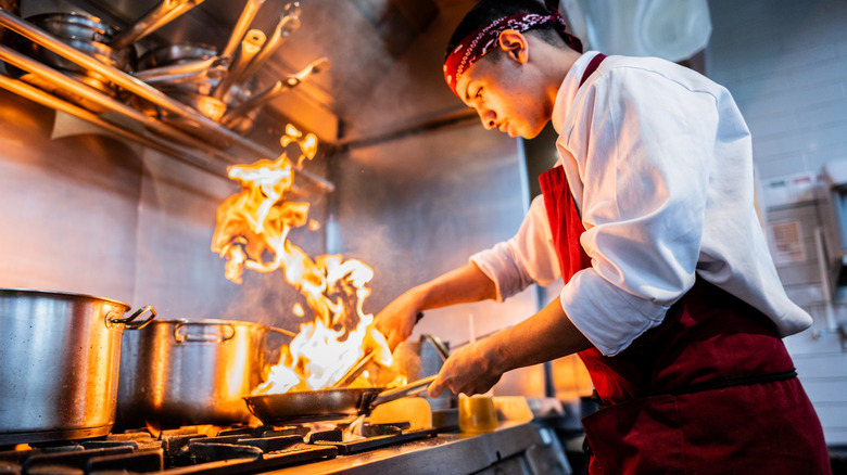 A chef cooks with flames on a commercial kitchen stove