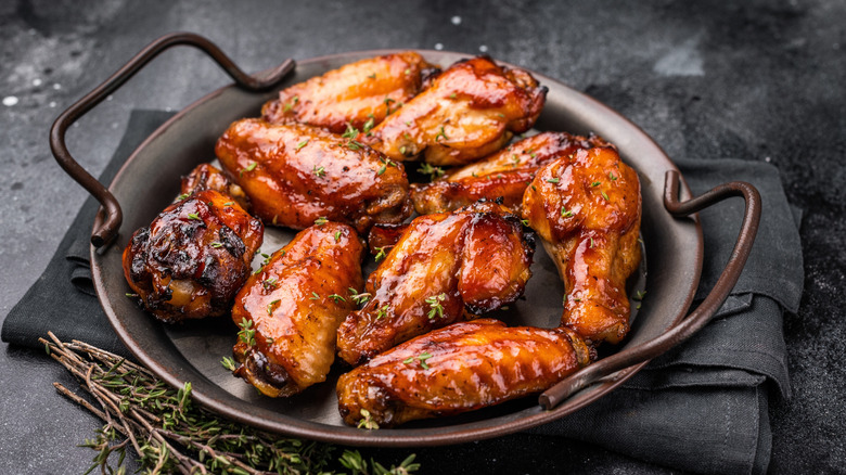Pieces of chicken covered in BBQ sauce on a black metal plate