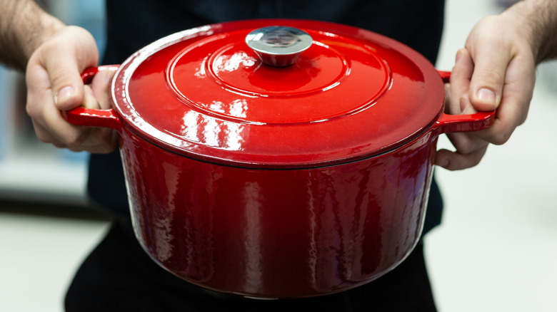 A person holds a bright red enameled Dutch oven