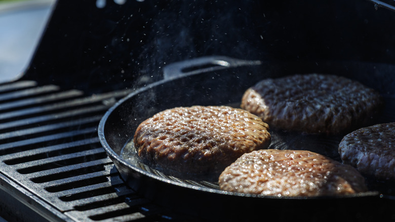 Burger patties being cooked on a cast iron skillet over grill.