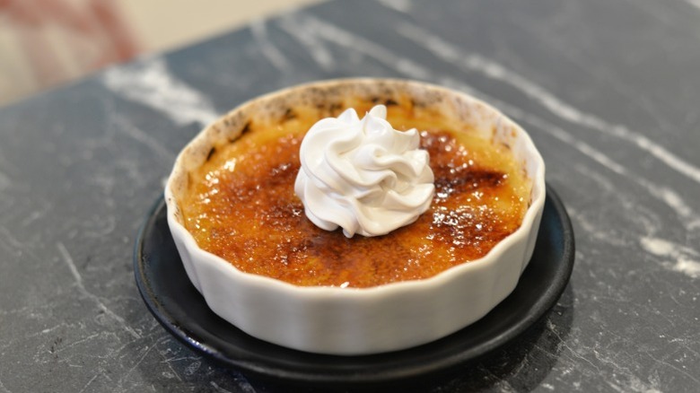 A shallow ramekin of creme brulee with a dollop of whipped cream on top.
