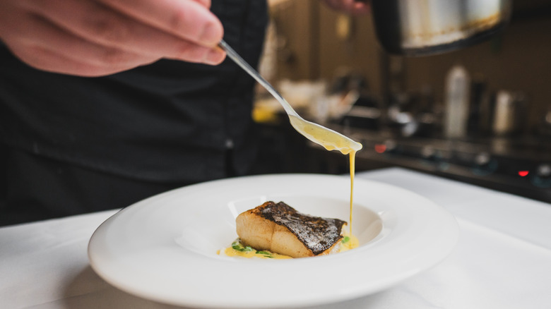 Chef adding sauce to fish dish