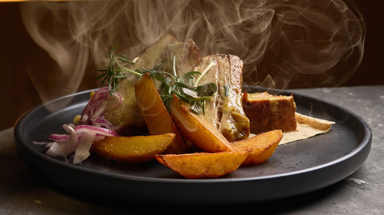 Steaming potato wedges and meat on black restaurant plate