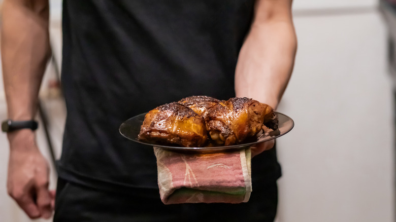 Person in black shirt holding black plate of roasted chicken with a towel