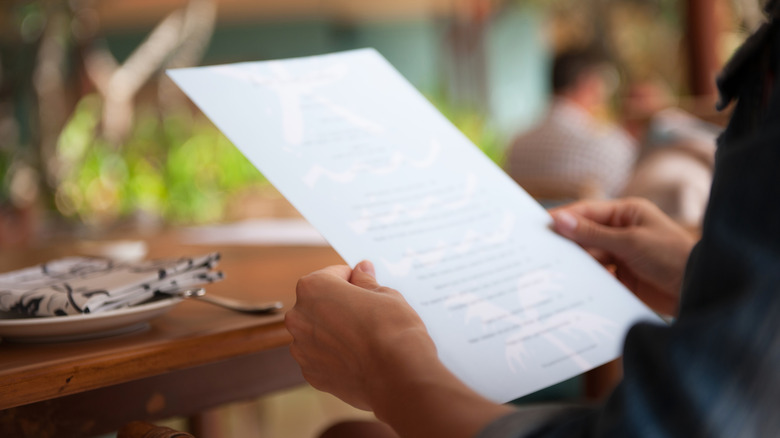 Person sitting at an outdoor table holds a single-page restaurant menu