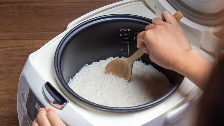 hand scooping rice from rice cooker using wooden spoon