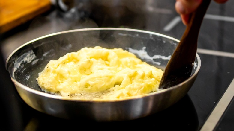 Person cooking scrambled eggs in pan on stove