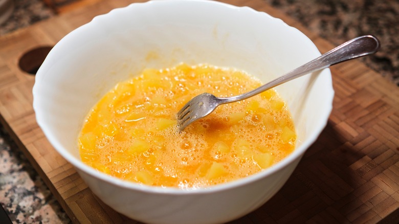 Whisked eggs and fork in white bowl