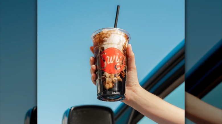 A Swig "dirty soda" being held from the window of a car.