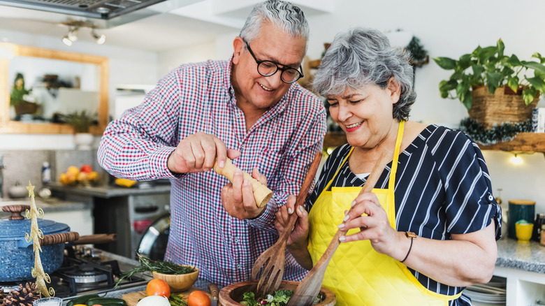 An elderly couple cooking together in a decorated kitchen.