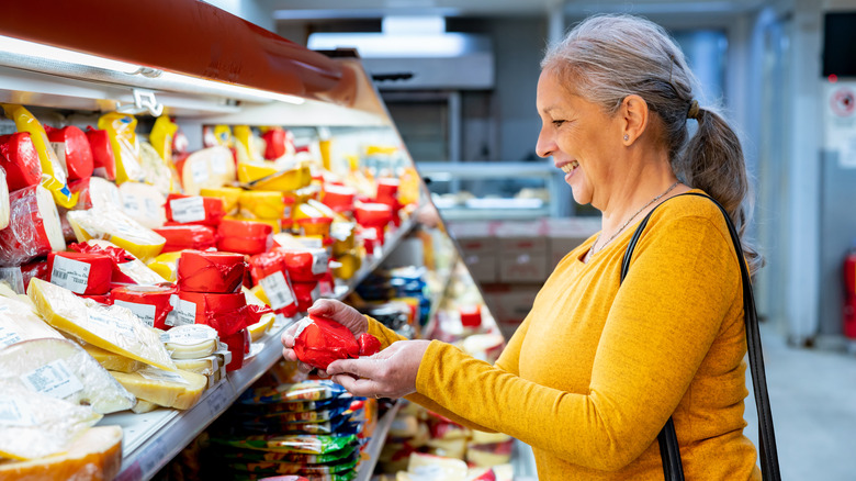 Cheerful senior woman looking at the label on a block of cheese she likes