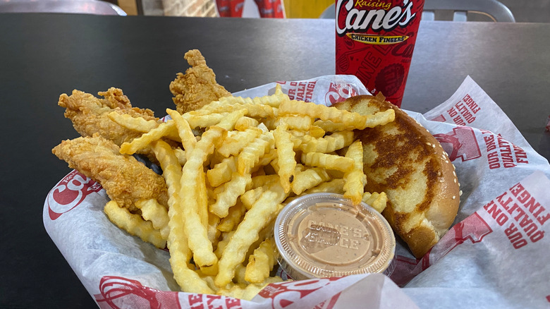 A meal from Raising Cane's consisting of crinkle cut fries, chicken tenders, toast, and sauce