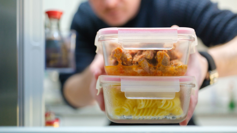 Man taking cooked pasta and chicken leftovers from the refrigerator.