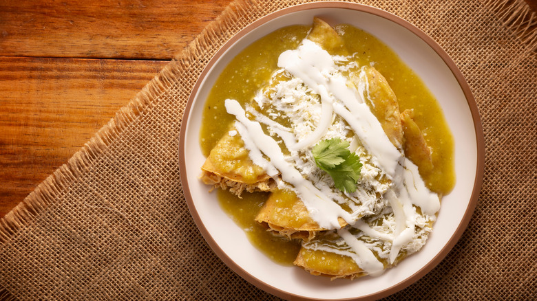 A plate of tacos with Mexican crema and green salsa on top
