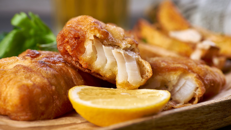 Beer battered fish fillets on a wooden dish with a slice of lemon