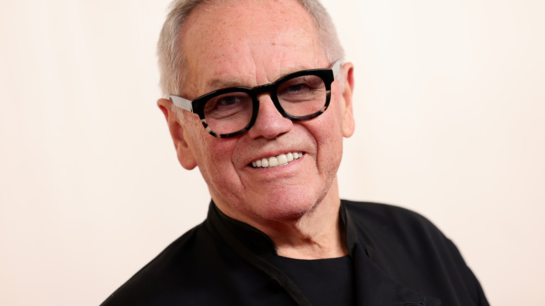 Wolfgang Puck smiles in glasses and a black chef's jacket at an event