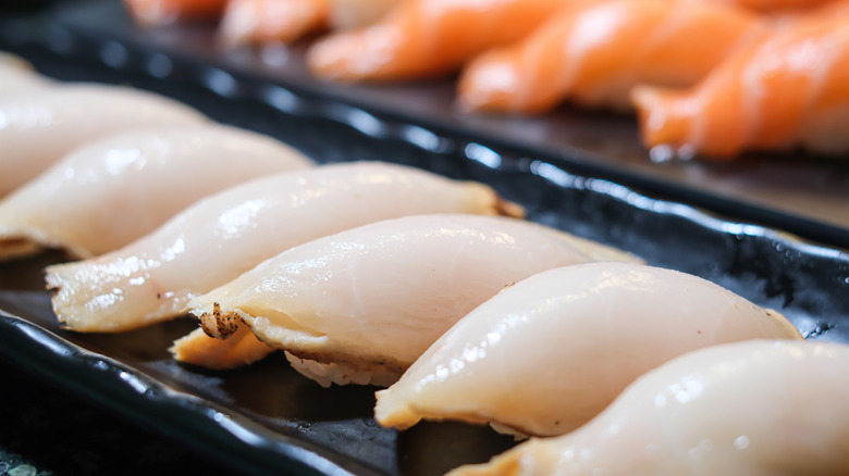 A row of escolar nigiri on black plate
