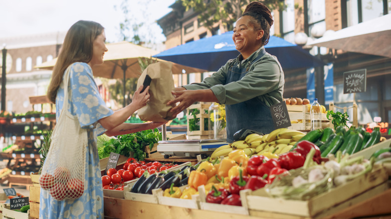 A woman buys produce at a farmer's market stand