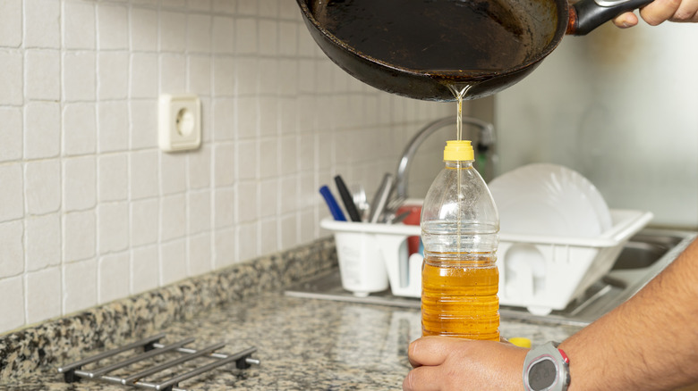 A hand pours grease from a pan into a plastic bottle on a kitchen counter