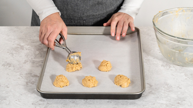 A person scooping cookie dough onto a parchment paper lined baking tray