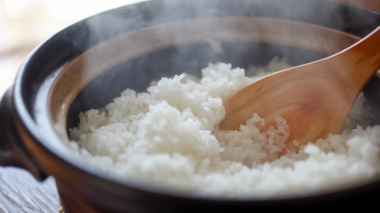 A rice cooker steaming with rice inside and a wooden spoon