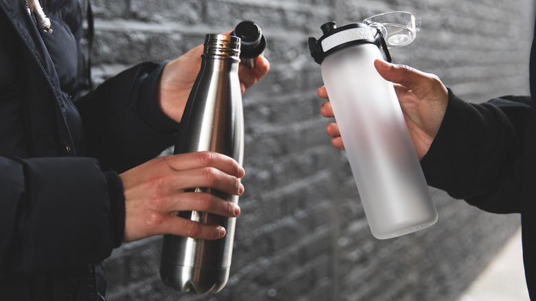 Two people holding water bottles made from different materials.