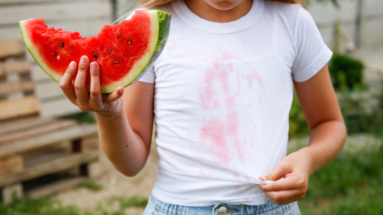 person with stained white shirt eating watermelon