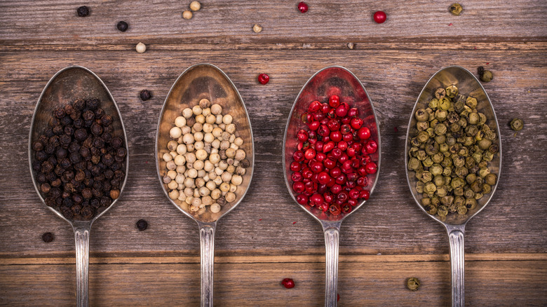 four kinds of whole peppercorns in spoons