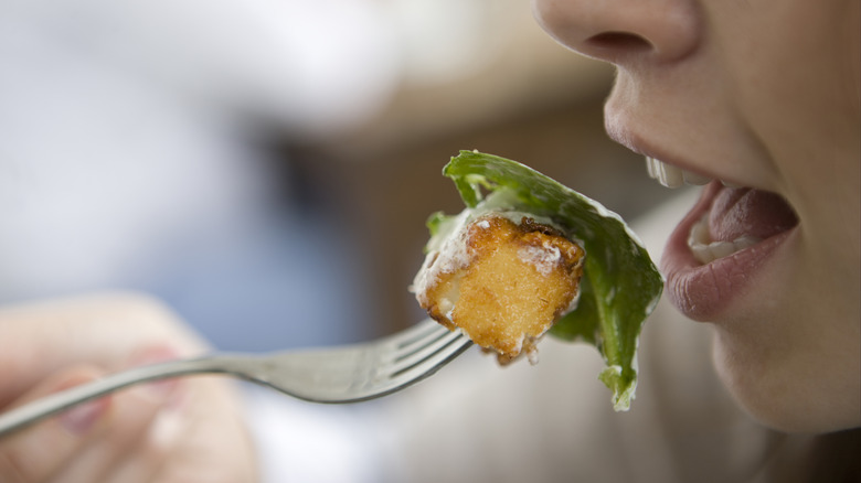 fork holding crouton and salad leaf approach open mouth