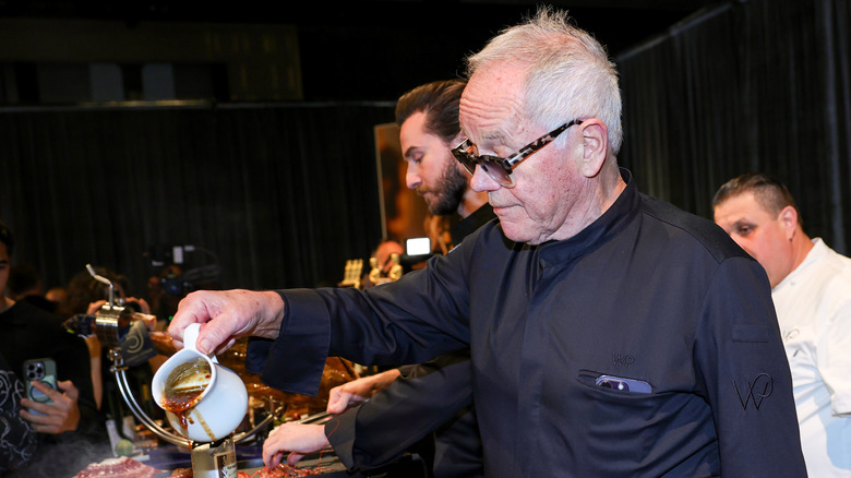 Wolfgang Puck pouring a brown sauce from a small ceramic pitcher