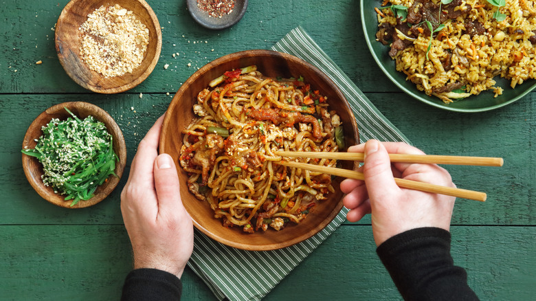 Top view of hands eating noodles with wooden chopsticks