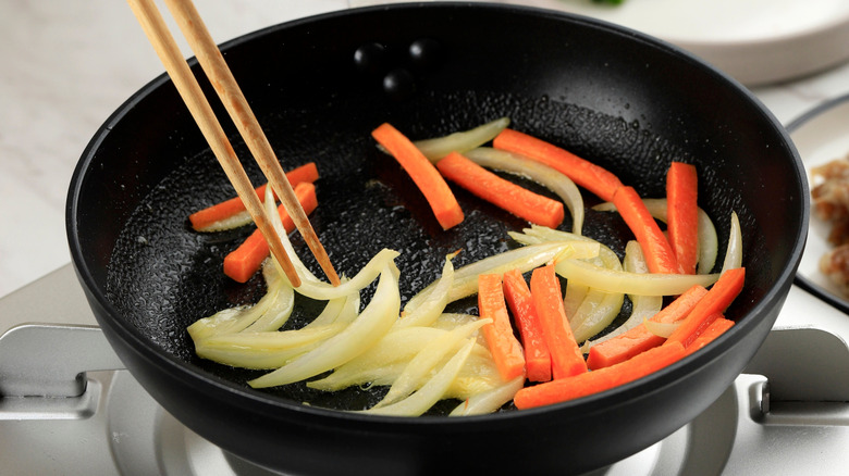 Someone stir-frying vegetables with wooden chopsticks
