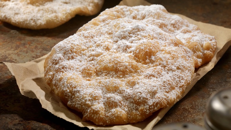 Fried dough dusted with powdered sugar on brown paper