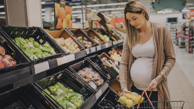 Pregnant woman putting produce in grocery carrier