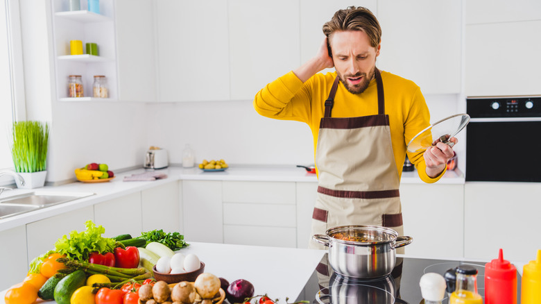 A man in a kitchen gives a dismayed reaction to the contents of his pan