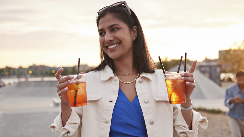 Smiling woman looking away while walking with cocktail drinks at sunset.