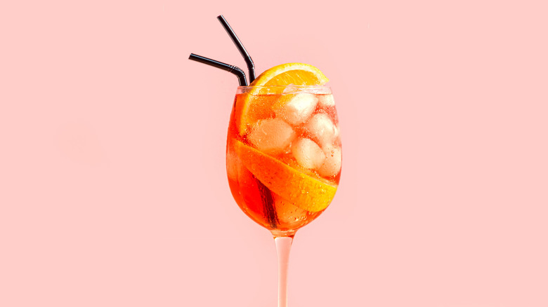 Aperol Spritz Cocktail in glass with orange slices on pink peach background.