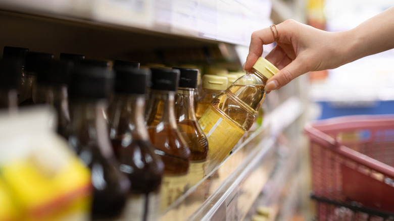 A woman takes a bottle of vinegar from a supermarket shelf