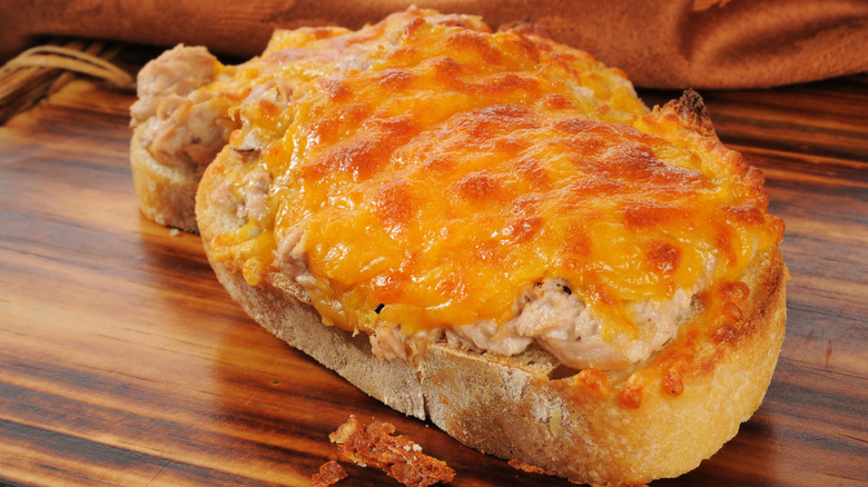 An open face tuna melt sandwich on a wooden board.