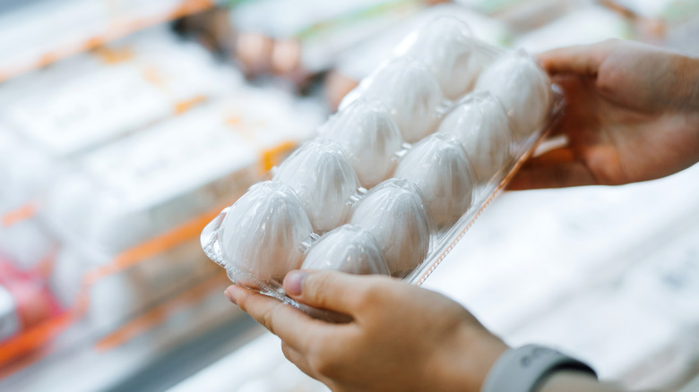 Two hands holding plastic carton of white eggs in grocery store
