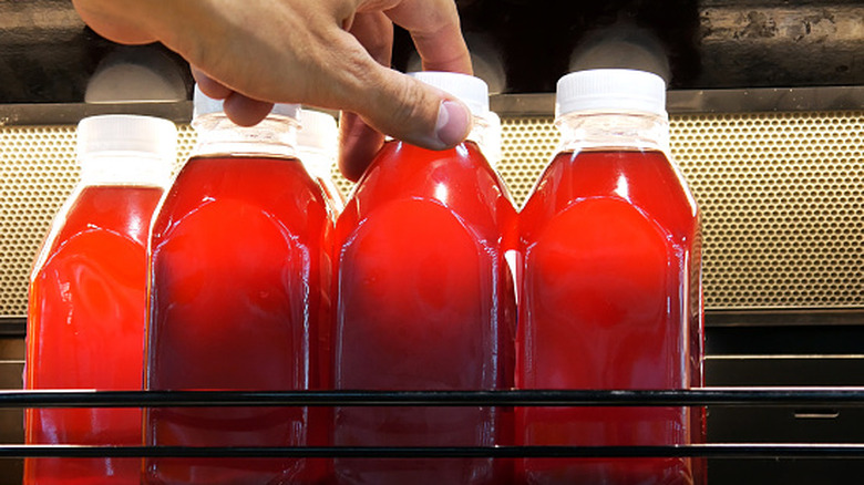 Bottles of berry juice on a refrigerated store shelf with a hand grabbing one.