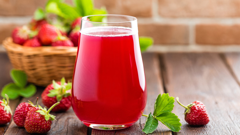 Strawberry juice in a glass with small strawberries surrounding it