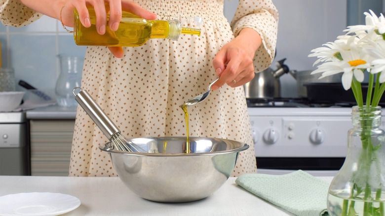 A home cook adds olive oil to a recipe in a metal bowl