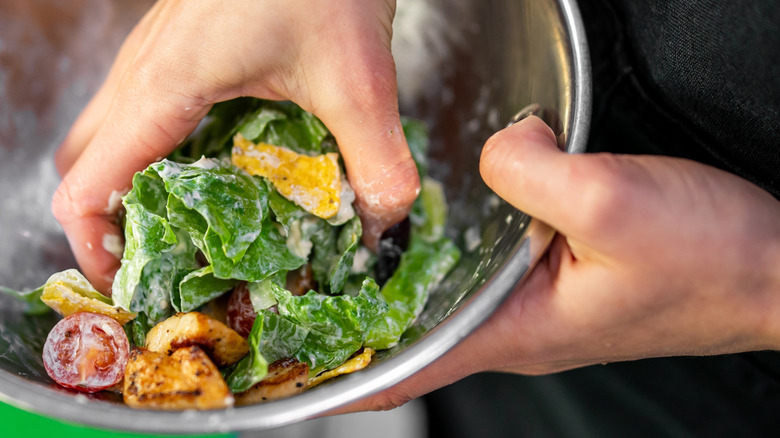 hands mixing creamy salad in metal bowl