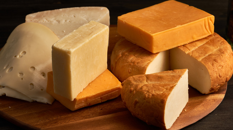 Various sliced cheese, cheese blocks, and whole cheese on a wooden board