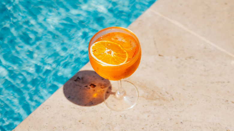 A glass of aperol spritz next to a pool