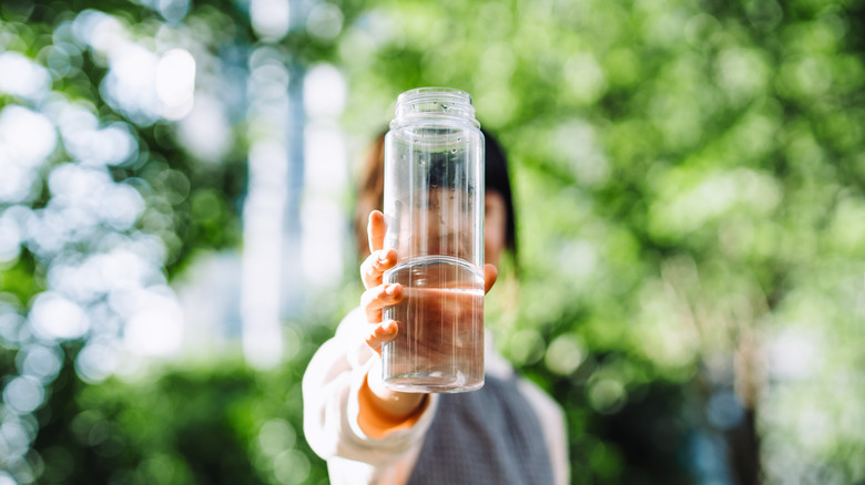 A person holding a bottle of water, covering their face