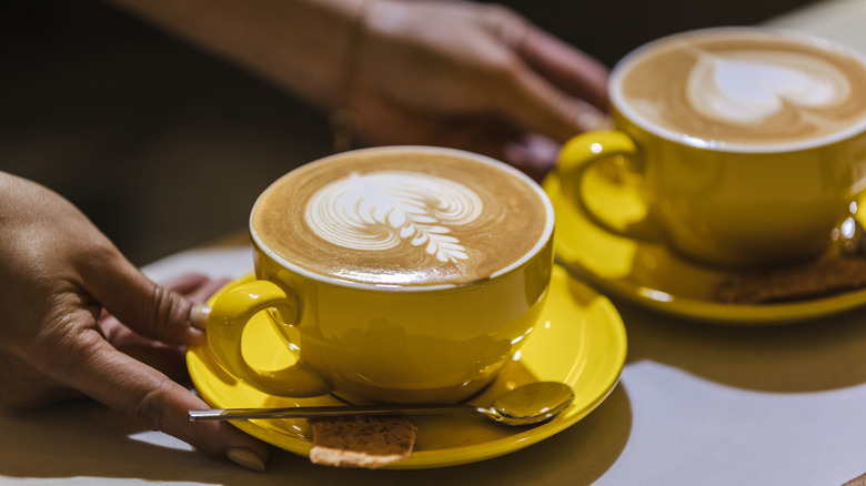 Barista hands serving two mugs of latte at coffee shop.