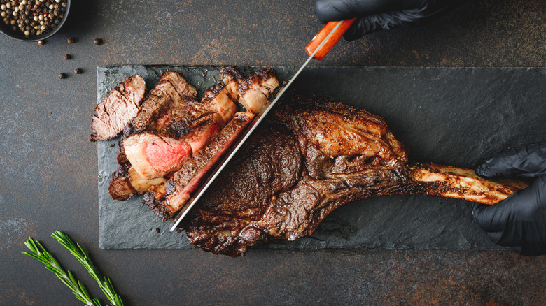 A chef cuts a grilled tomahawk steak