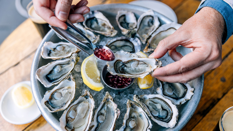 Hands spooning sauce onto an oyster.